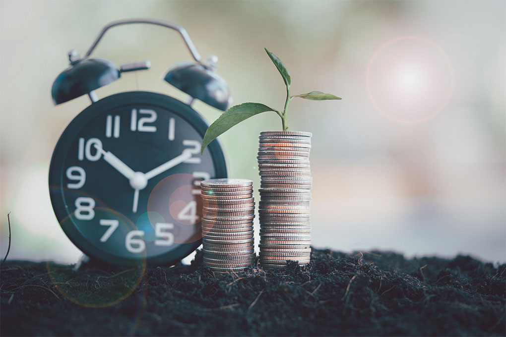 Black clock with coins and growing green plant