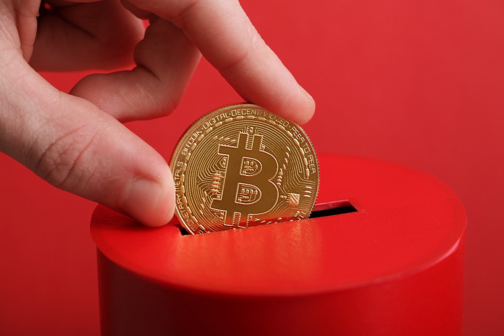 A person deposits a bitcoin in a piggy bank.