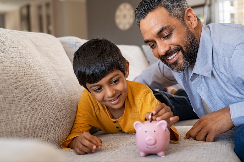 A man and his son putting a coin in a piggy bank.