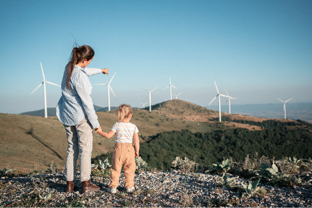 A picture of a woman and her young daughter looking at a landscape with wind turbines.