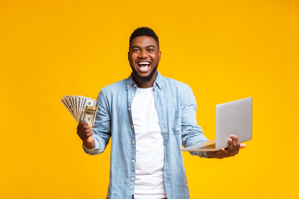 Happy man holding money and his computer in his hands