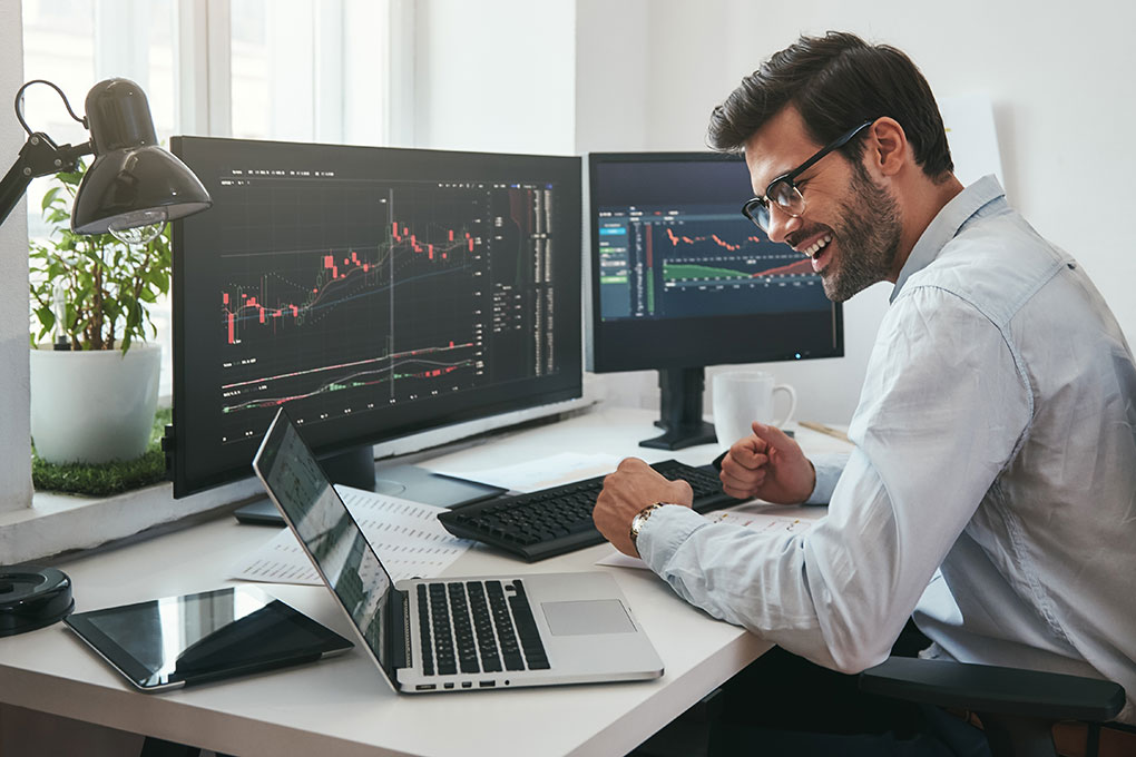 Smiling man in front of a screen looking at stock charts after an option trade