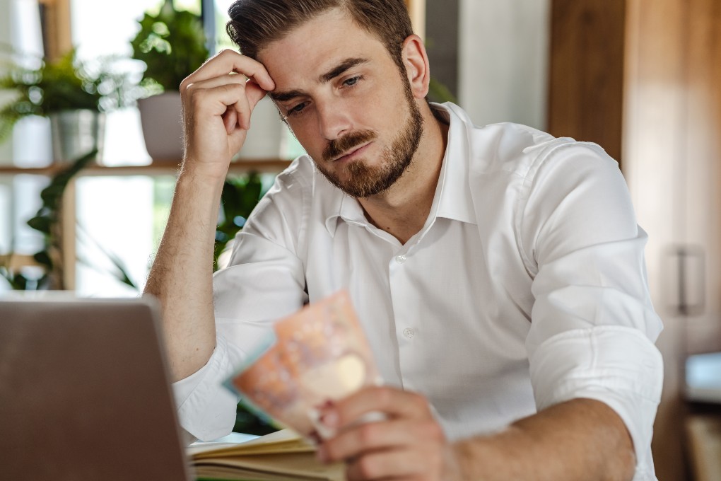 A preoccupied man in front of a computer looks at his money
