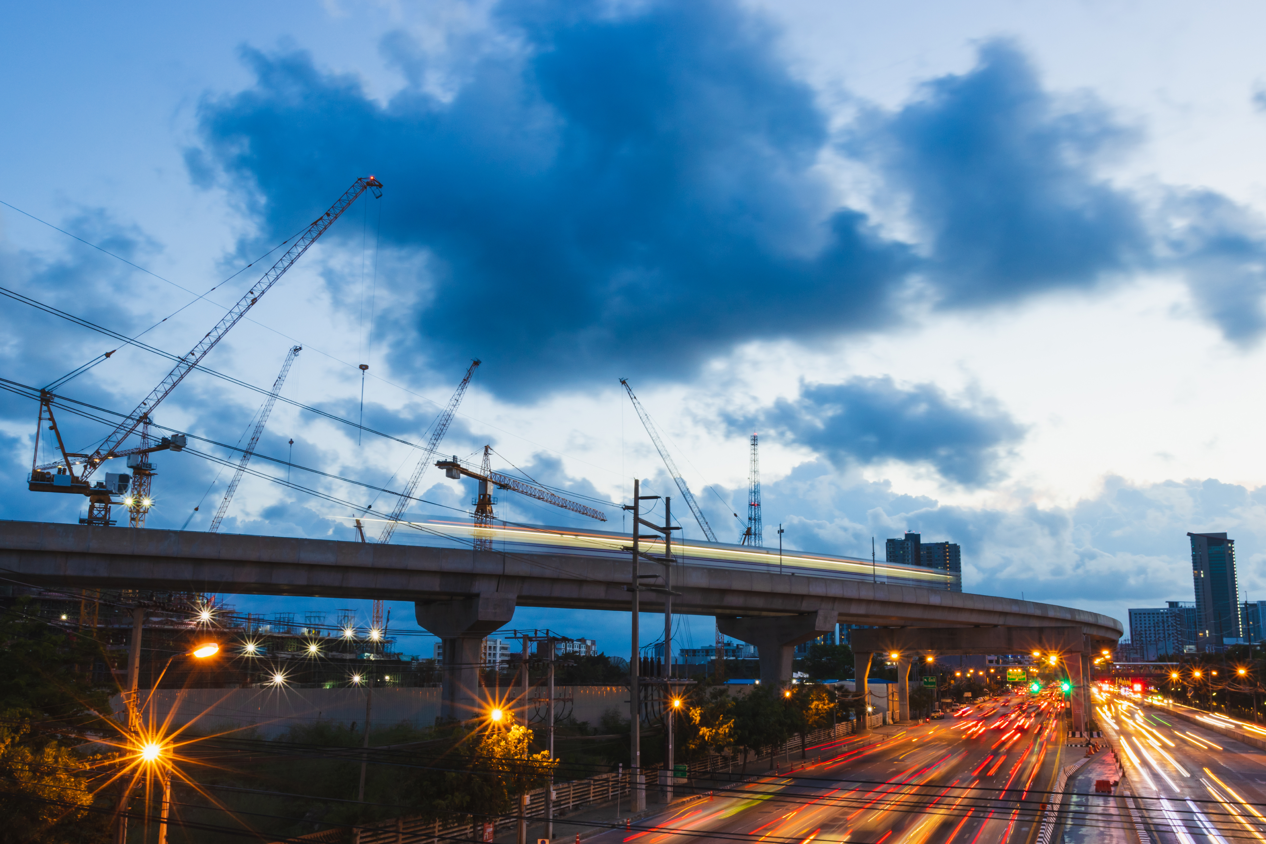 Elevated overpass, cranes and cars under cloudy sky