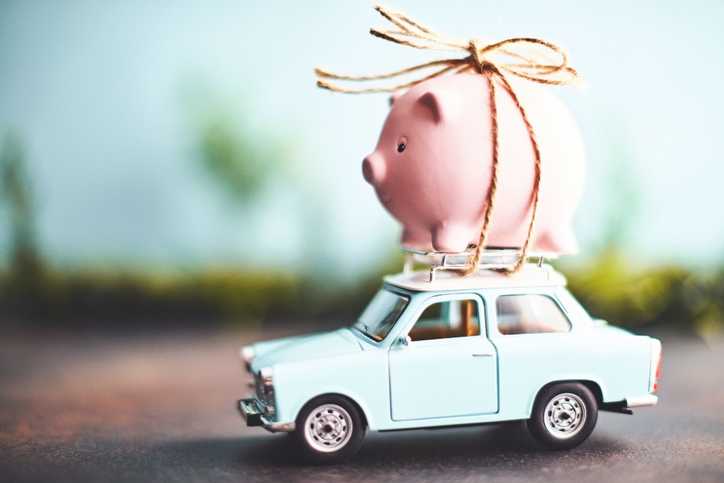 A pink piggy bank is attached to the roof of a small car.
