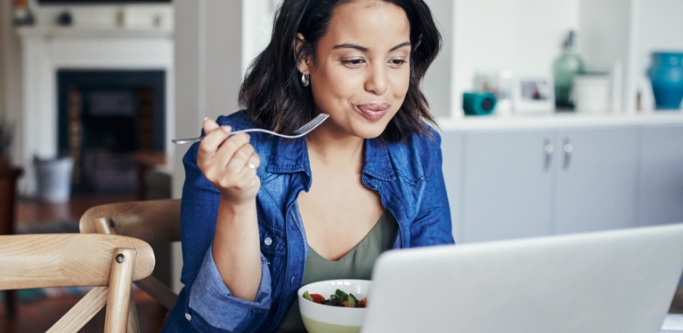 Photo d’une femme qui regarde son ordinateur en mangeant dans sa cuisine