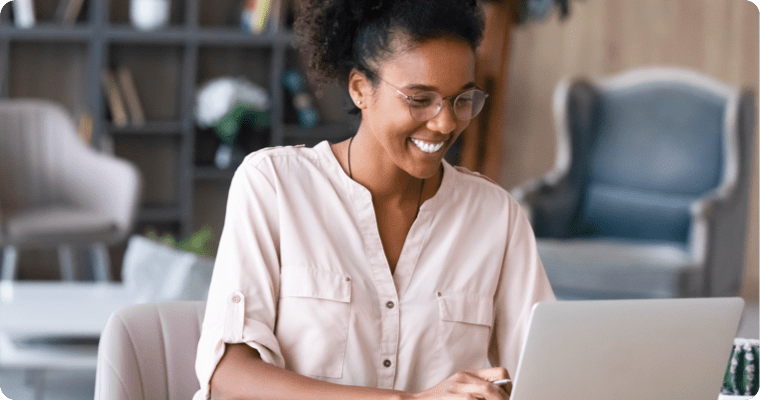 Photo of a smiling woman at her laptop in her kitchen