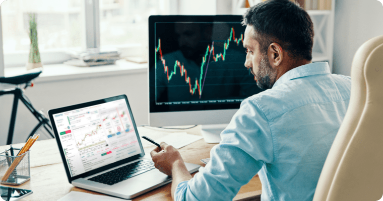 Photo of a man looking at charts on their two computer screens